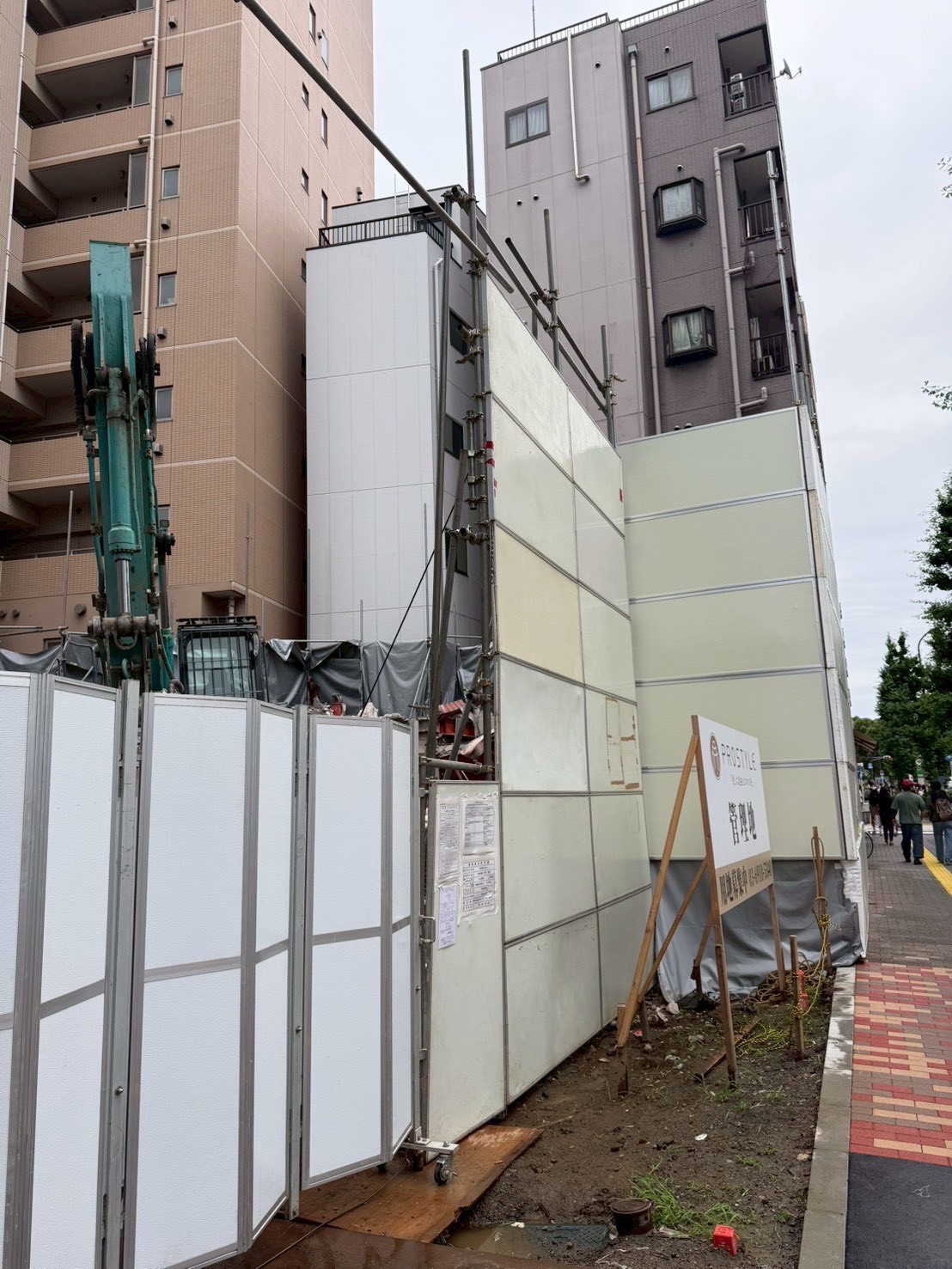 防音パネルの内側で散水しながら進めるビル解体工事の重機作業
